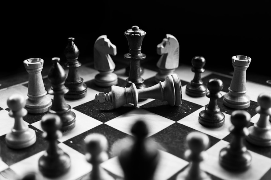 Chess pieces on a board, a fallen king among them